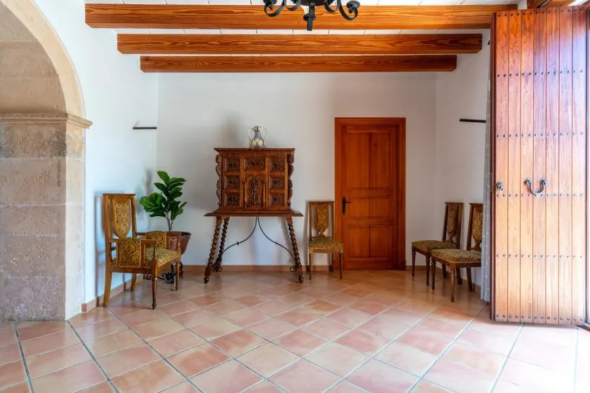 A tiled room with wooden beams, chairs, and a carved cabinet.