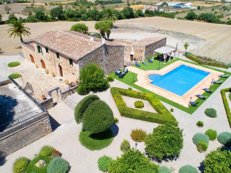 An aerial view of a stone building beside a swimming pool and landscaped garden.