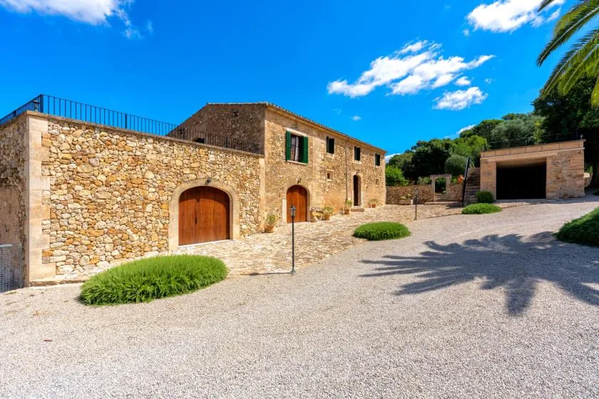 A stone building and courtyard with arched wooden doors and a gravel drive.