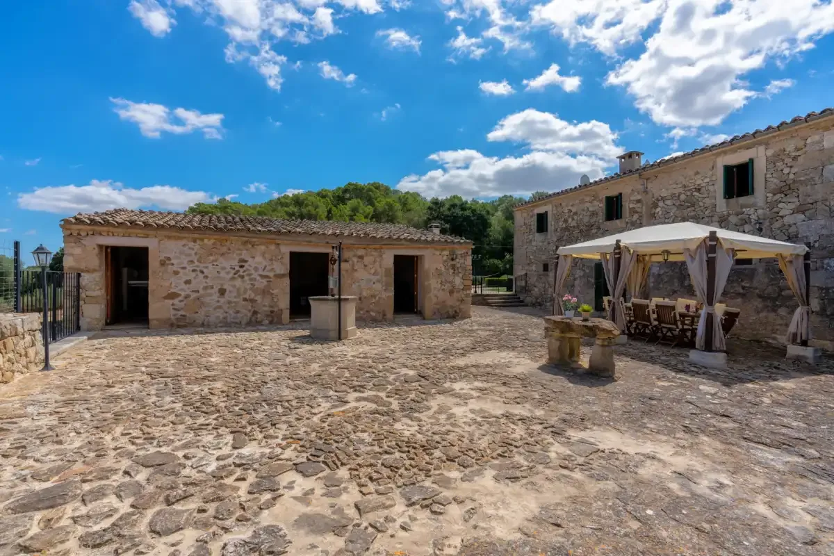 A stone courtyard with a covered outdoor seating area beside rustic buildings.
