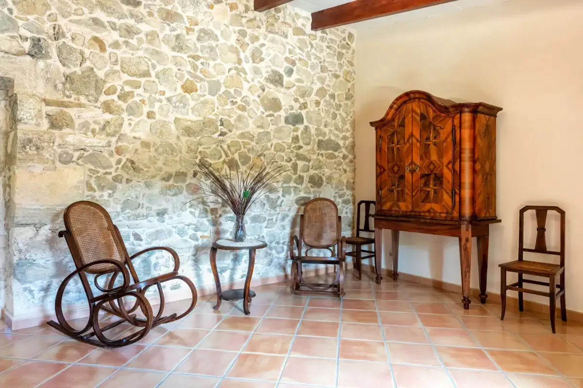 A rustic sitting room with stone walls, wooden furniture, and tiled floors.