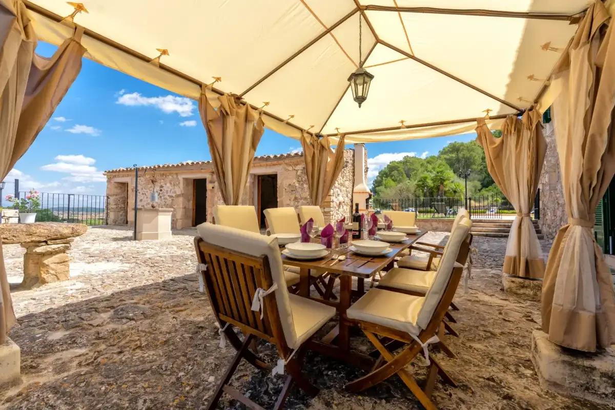 A covered outdoor dining area with a long table and cushioned seating.