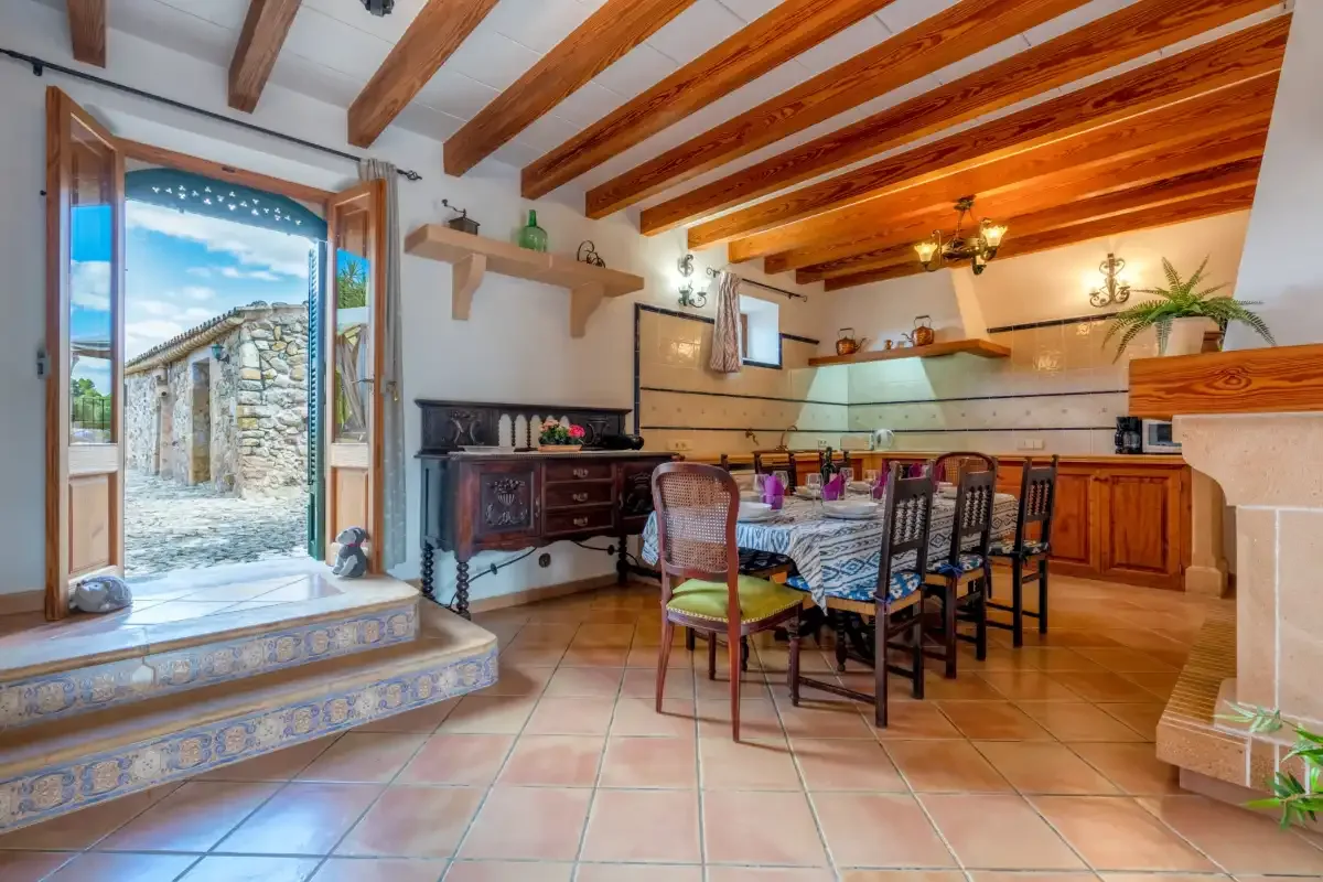 A rustic kitchen and dining area with a long table beneath exposed wooden ceiling beams.