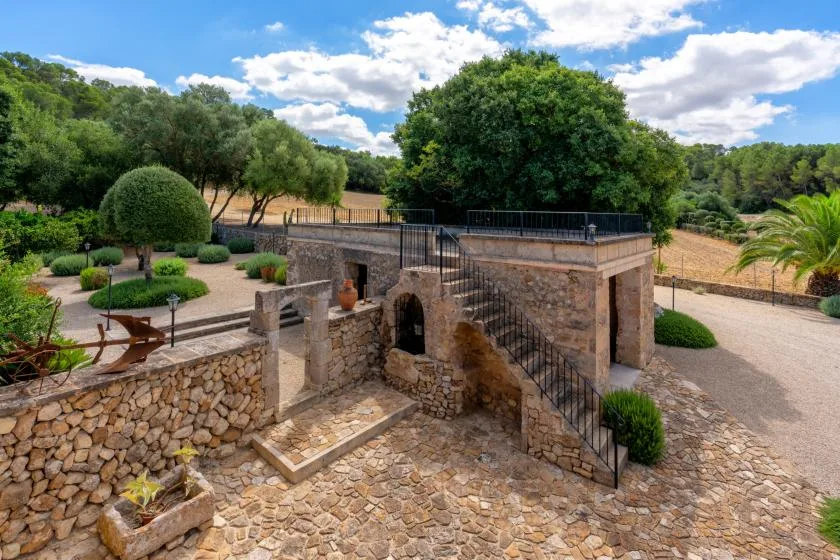 A stone garden terrace with steps, low walls, and trees.