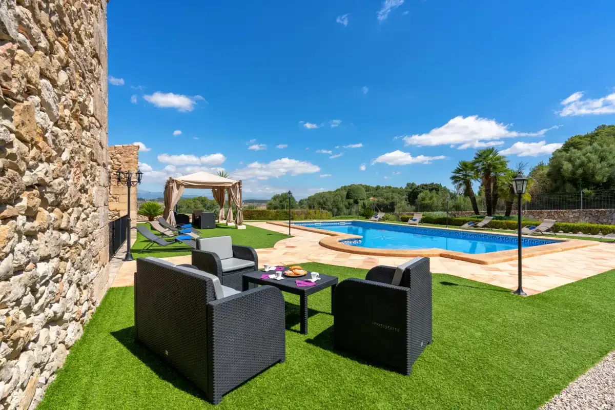 Outdoor seating on a lawn beside a swimming pool and stone wall.