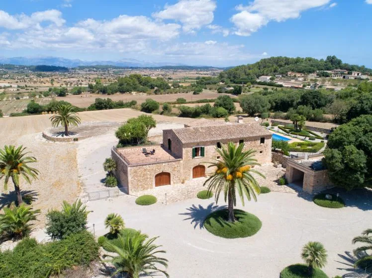 A stone building stands amid landscaped grounds, with palm trees and open countryside beyond.