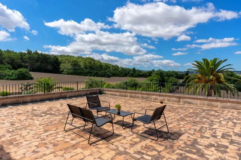 A paved outdoor terrace with seating overlooks a field and tree-lined landscape.