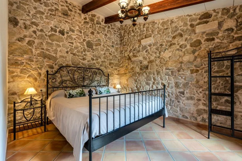 A bedroom with a metal bed against exposed stone walls.