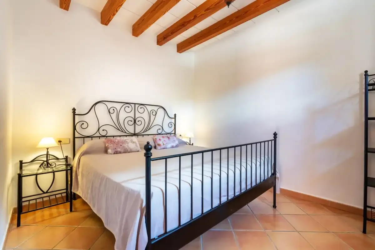 A bedroom with a metal bed beneath exposed wooden ceiling beams.