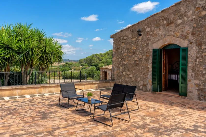 A sunny stone terrace with outdoor seating and an open doorway.