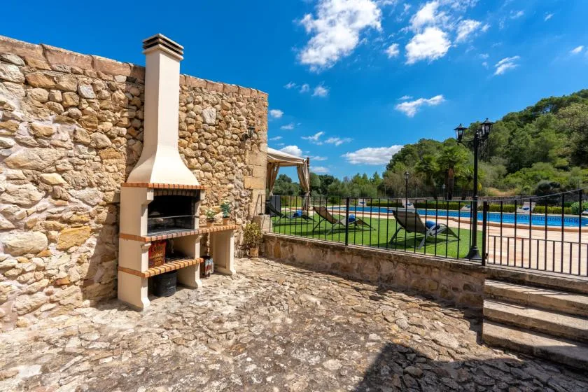 A stone outdoor patio with a built-in barbecue beside a fenced swimming pool.