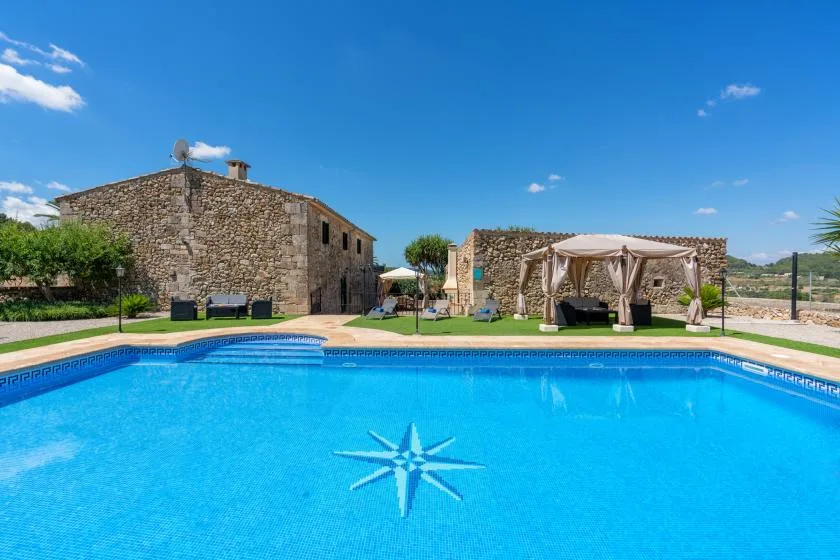 A swimming pool in front of a stone building and a shaded seating area.