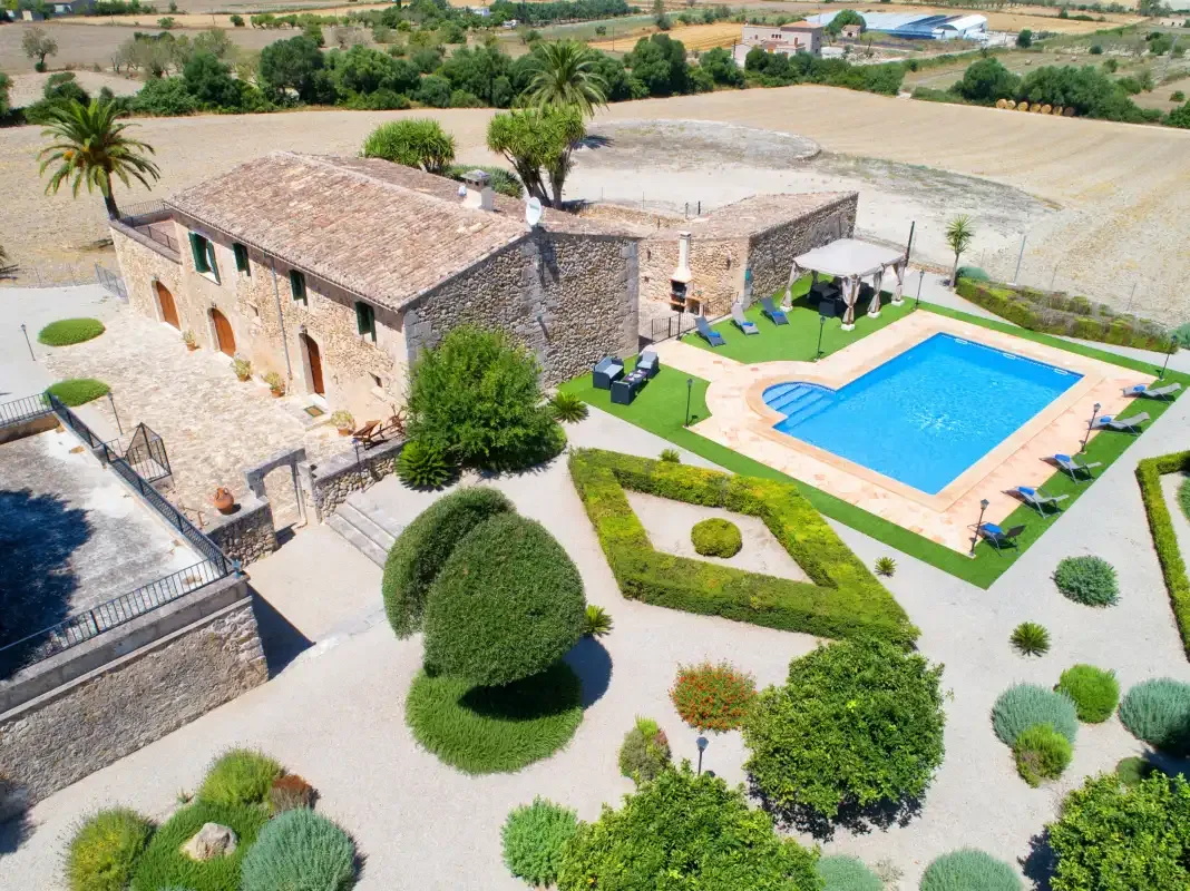 Aerial view of a stone building beside a swimming pool and landscaped grounds.
