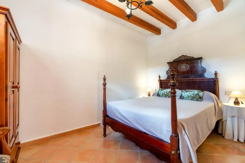 A bedroom with a wooden four-poster bed and exposed ceiling beams.