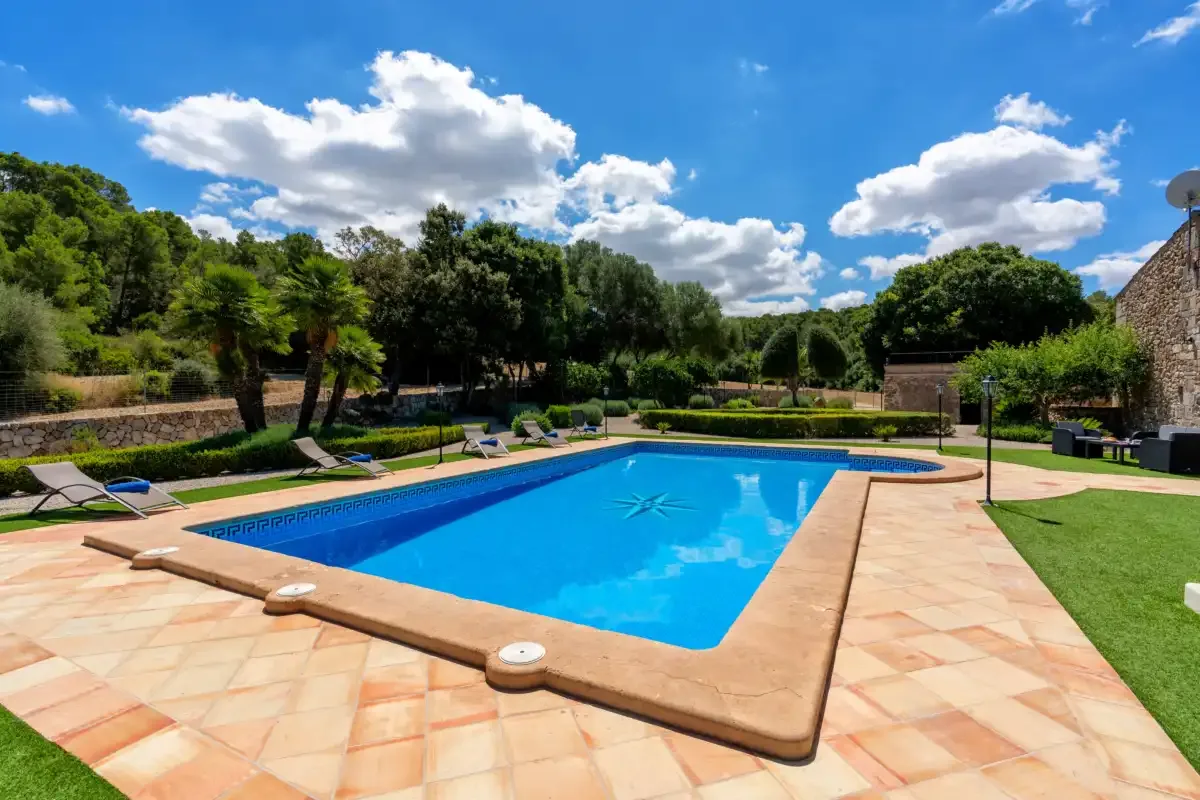 An outdoor swimming pool is surrounded by a tiled patio and greenery.