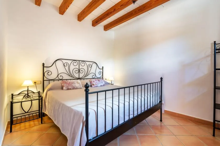 A bedroom with a metal bed, bedside tables, and exposed wooden ceiling beams.