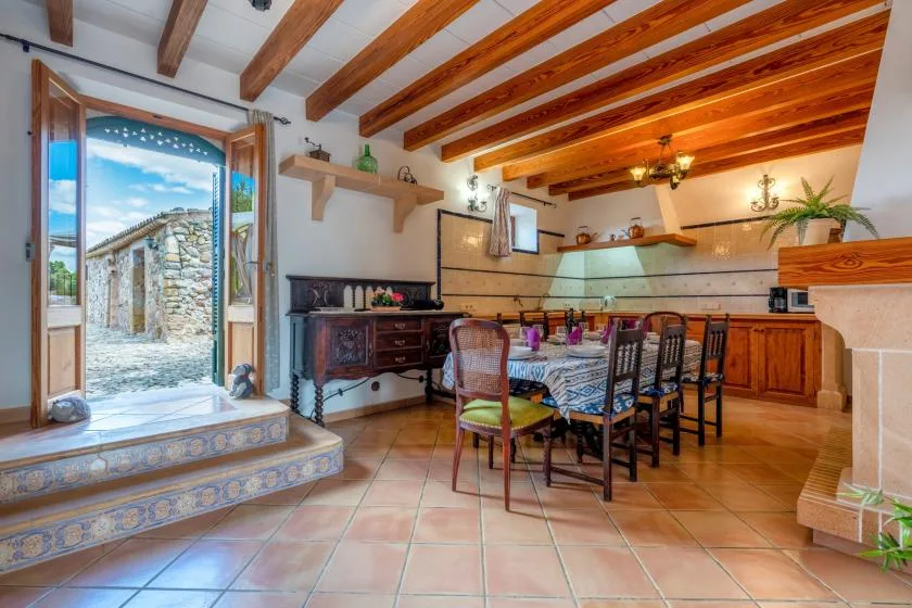 A rustic kitchen and dining area with a long table beneath exposed wooden ceiling beams.