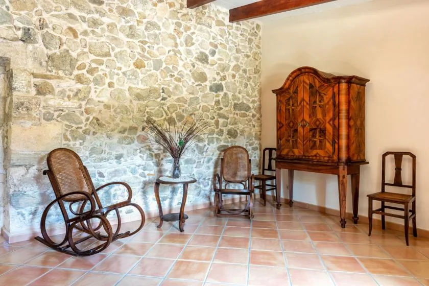 A rustic sitting room with a stone wall, wooden cabinet, and seating.