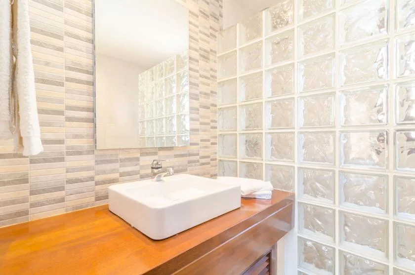 A bathroom vanity with a white basin beside a glass-block wall.