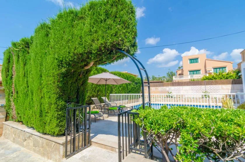 A poolside patio with lounge seating, an umbrella, and surrounding greenery.