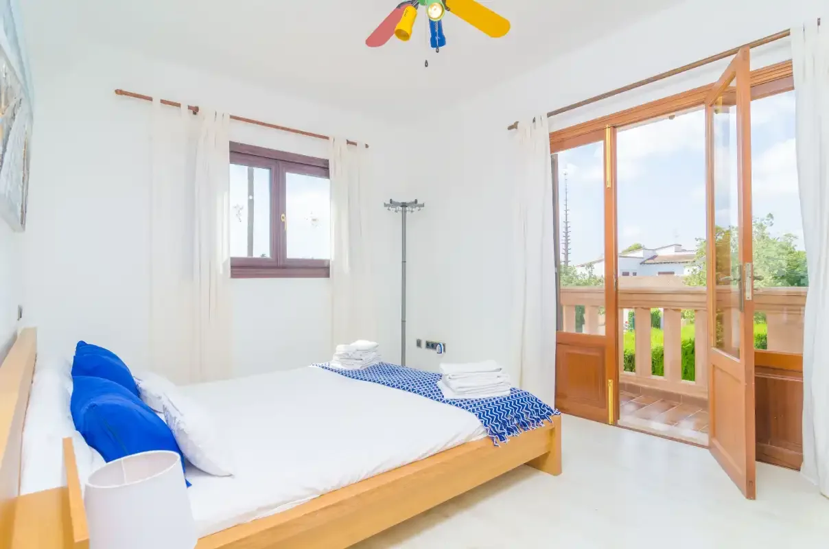 A bright bedroom with a neatly made bed beside open wooden balcony doors.