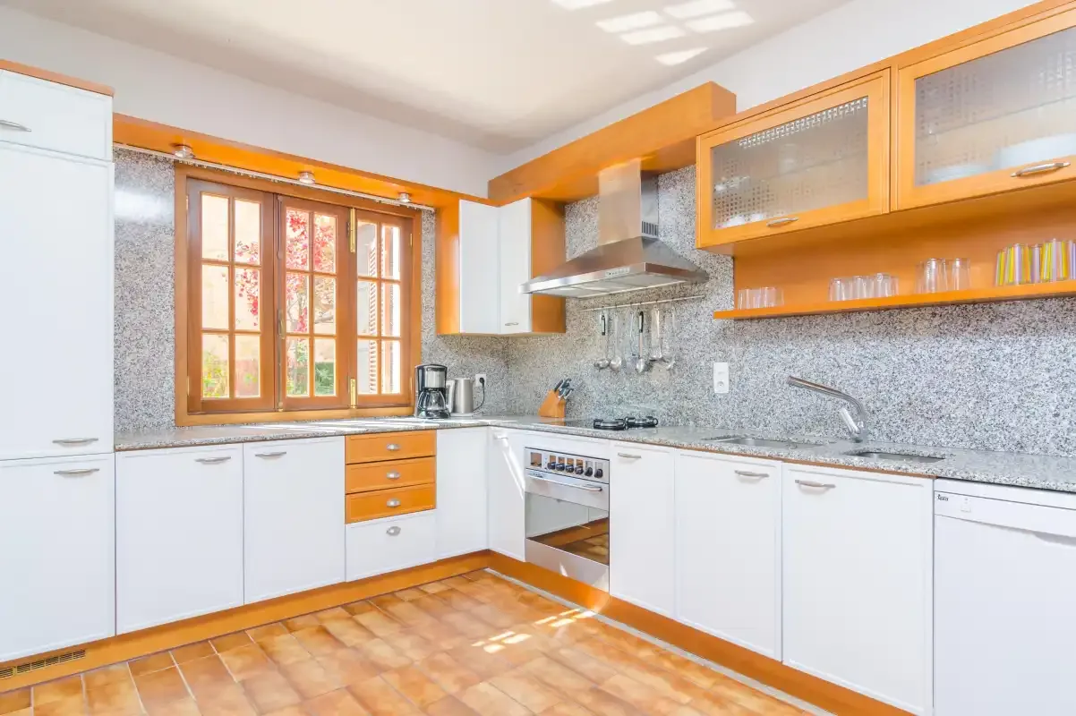 A bright kitchen with white cabinets, wooden trim, and a window above the counter.