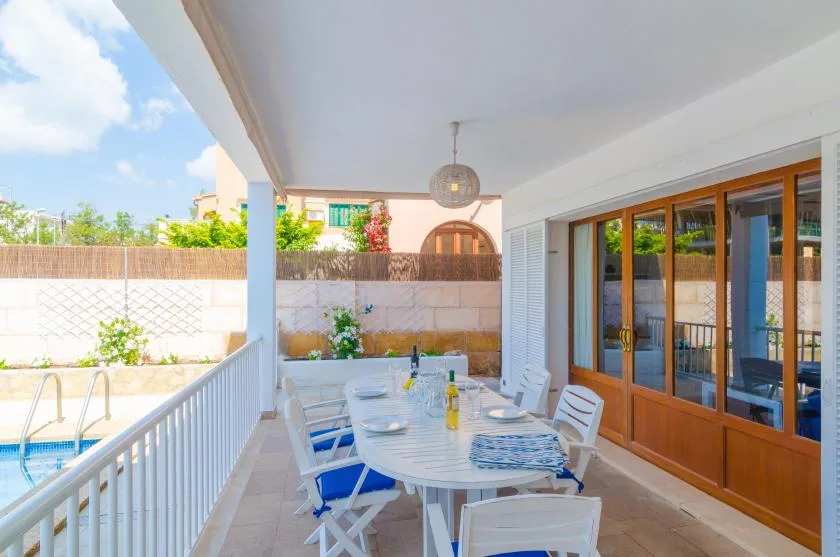A covered outdoor dining area overlooks a swimming pool, with a table and chairs.
