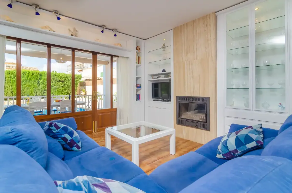 A bright living room with blue seating, a fireplace, and large glass doors.