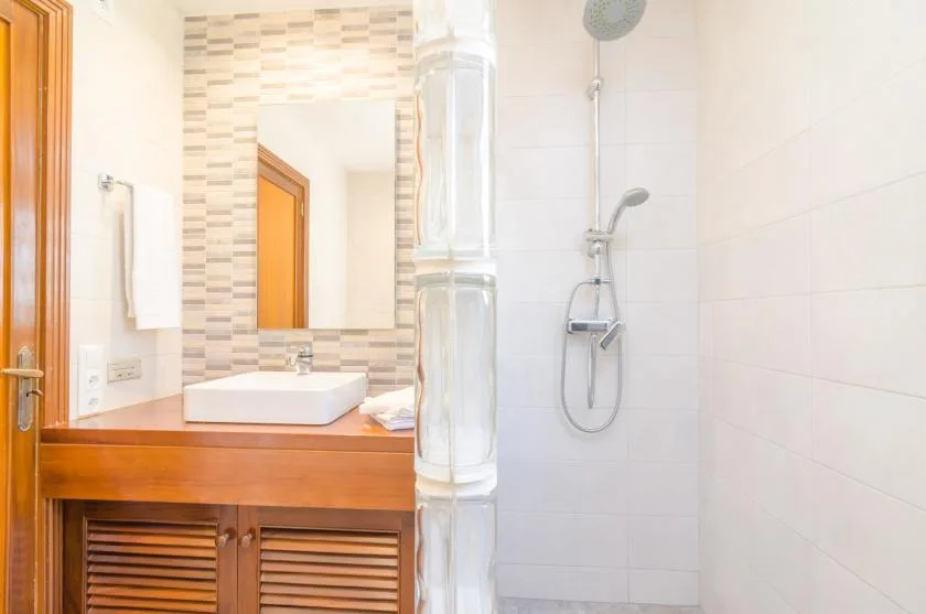 A bathroom with a sink and vanity beside a tiled shower.