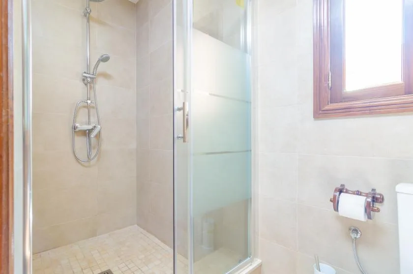A tiled bathroom with a glass shower and a wooden-framed window.