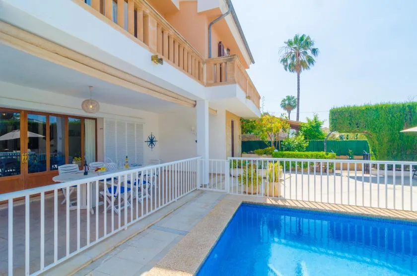 A swimming pool beside a house, with a patio dining area and garden hedges.