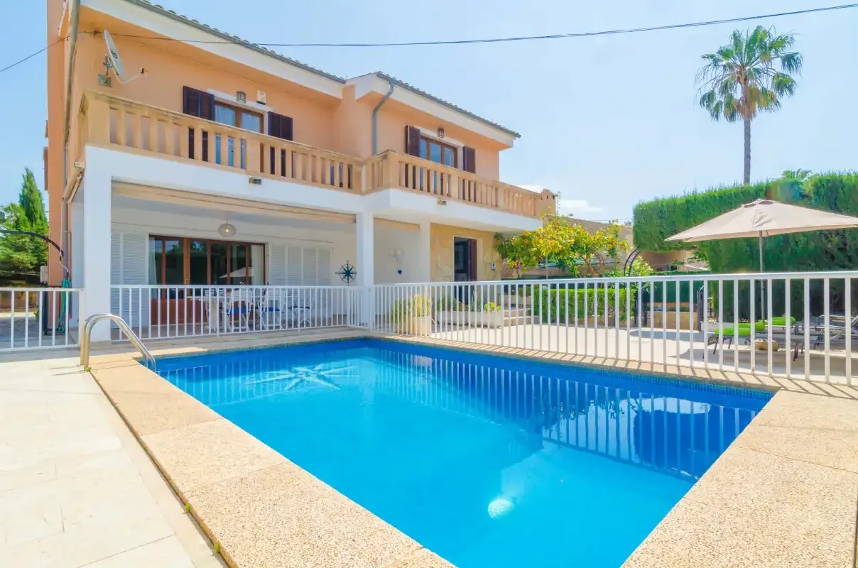 A swimming pool sits beside a two-story house with a covered patio.