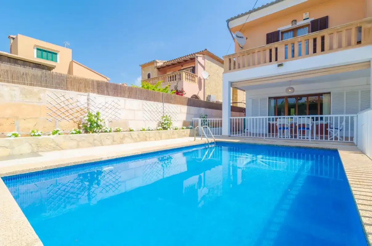 An outdoor swimming pool sits beside a house with a covered patio.