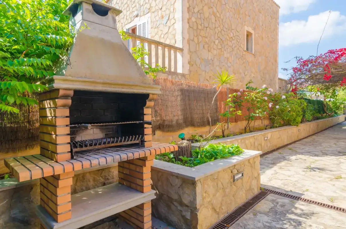 An outdoor barbecue grill stands beside a raised garden bed in a paved courtyard.