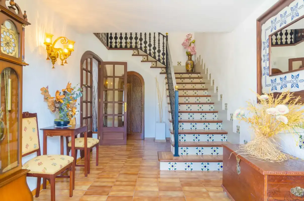 An entry hall with a tiled staircase, wooden furniture, and decorative wall details.