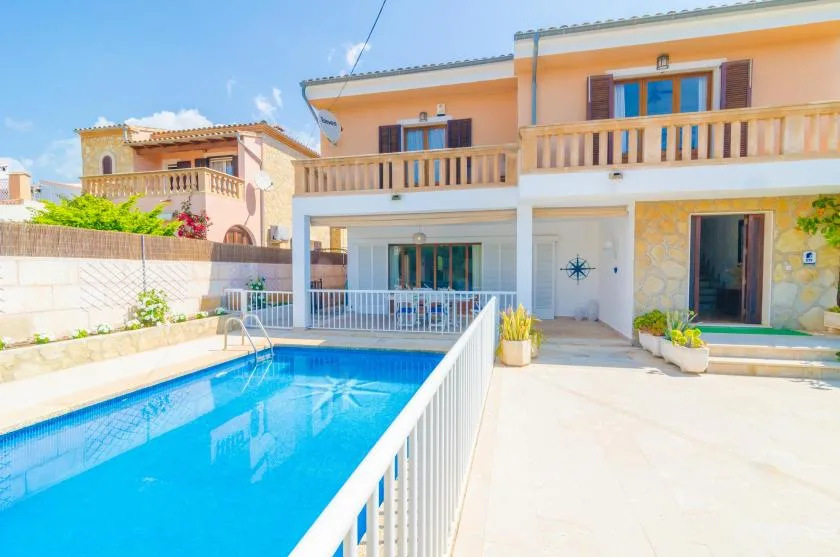 Una piscina junto a una casa de dos plantas, con balcón y patio.