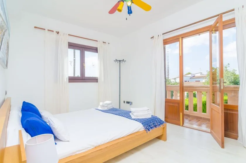 A bright bedroom with a bed beside open wooden doors leading to a balcony.