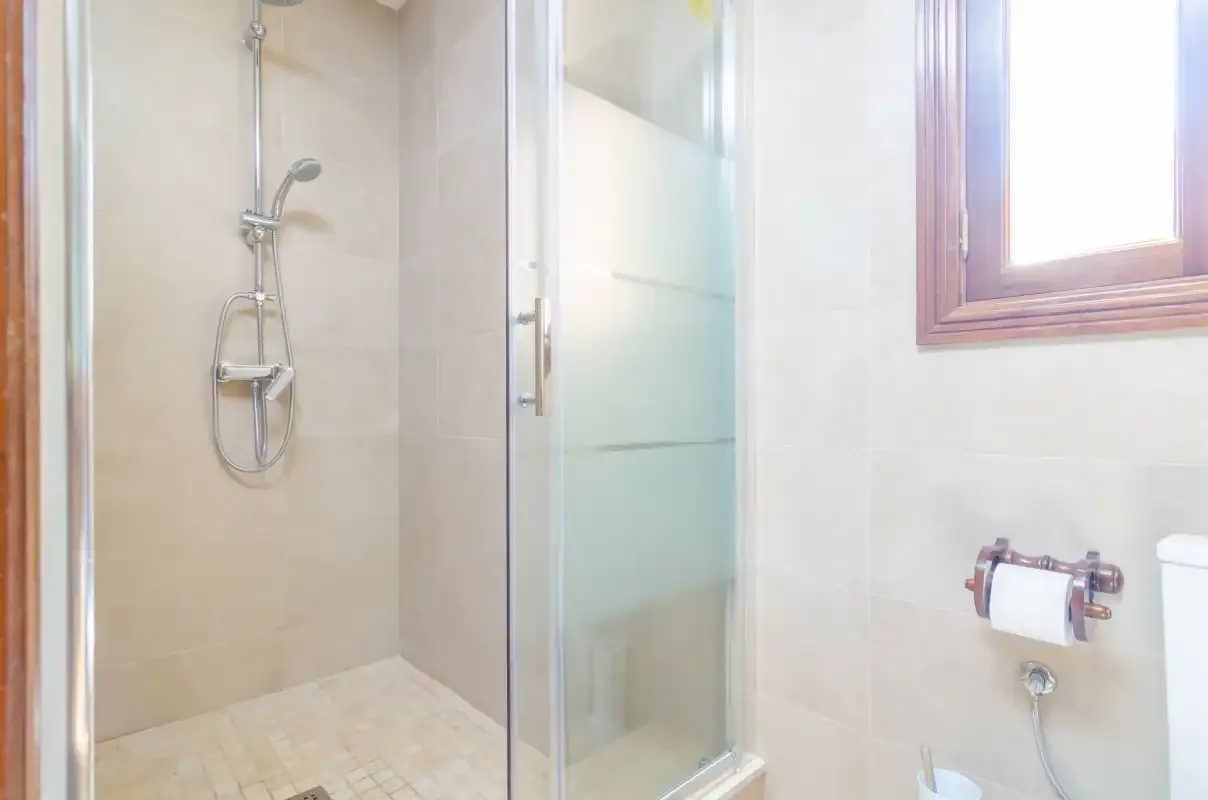 A tiled bathroom with a glass shower and a window.
