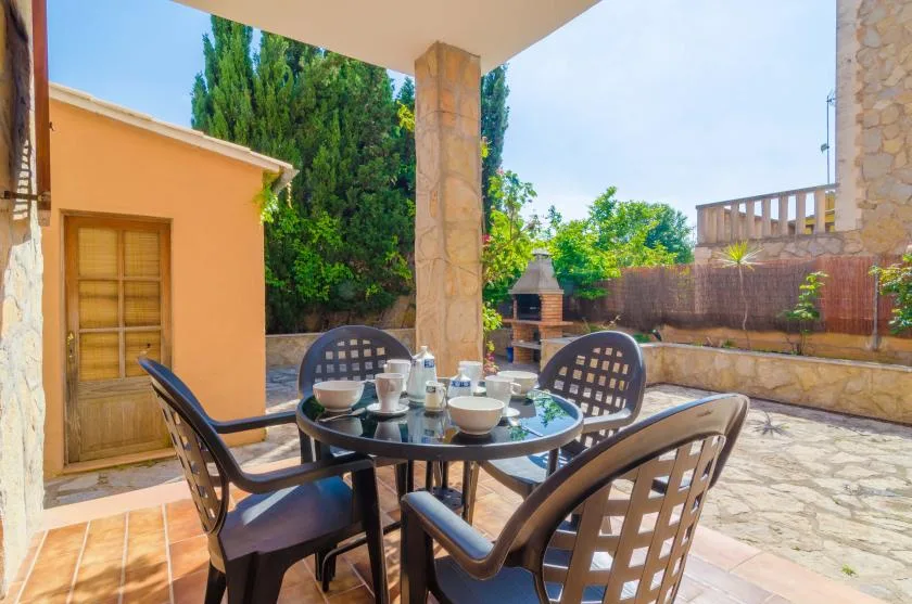 A covered outdoor dining area with a table and chairs overlooks a sunny patio.