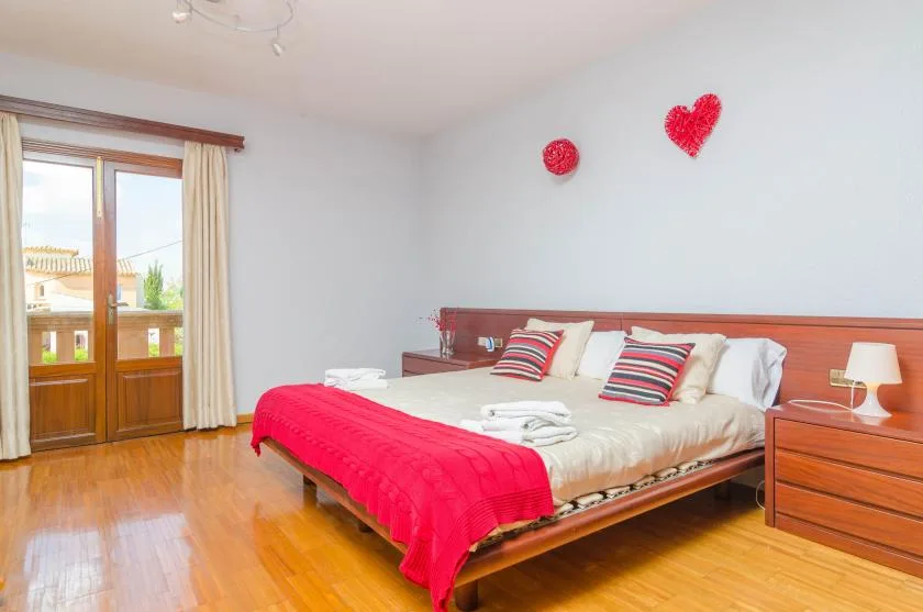 A bedroom with a bed dressed in white linens and a red cover.