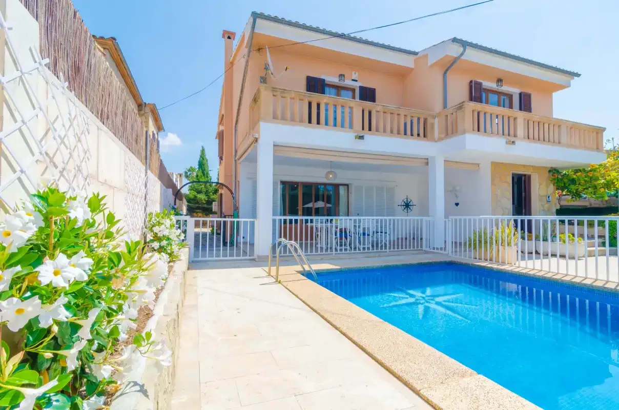 A two-story house stands beside a bright blue swimming pool and paved patio.