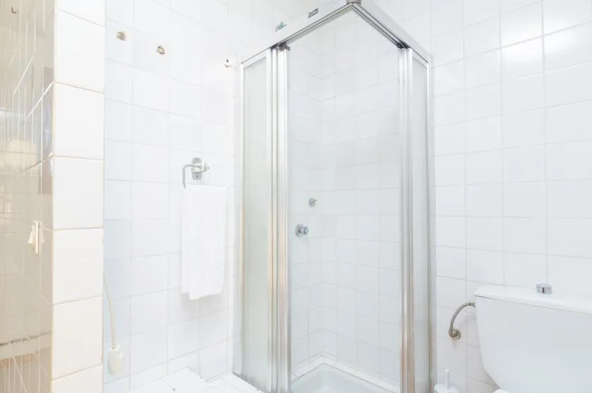 A tiled bathroom with a glass shower and a towel hanging on the wall.