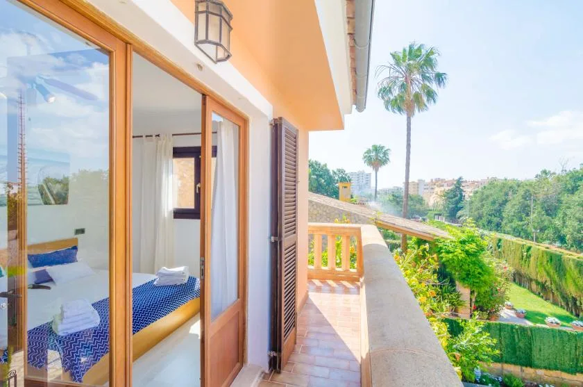 A sunny balcony beside an open bedroom, overlooking palm trees and greenery.