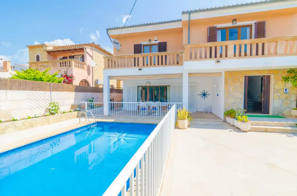 A sunlit house exterior with a swimming pool and terrace.