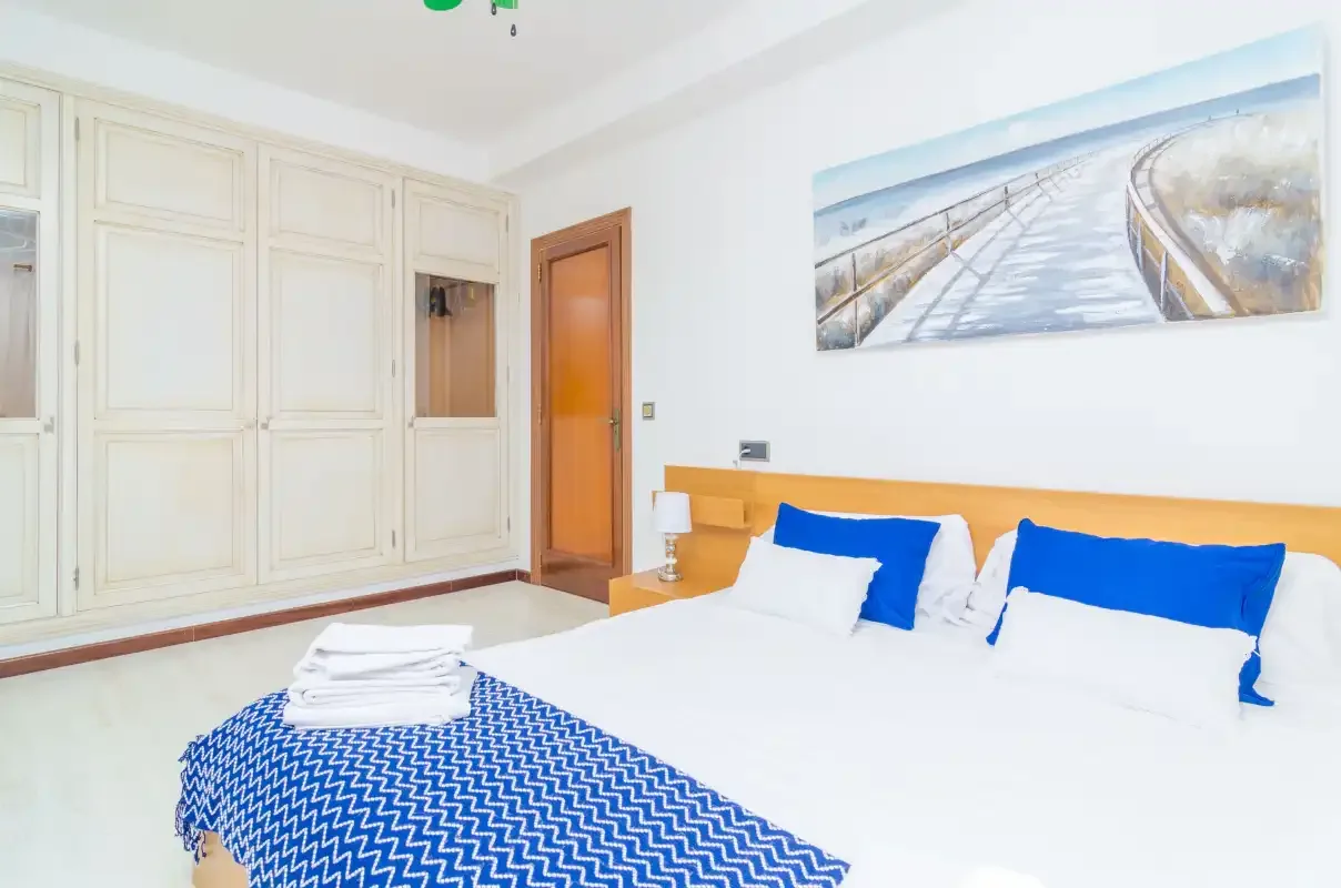 A bright bedroom with a bed, blue bedding, and built-in wardrobes.