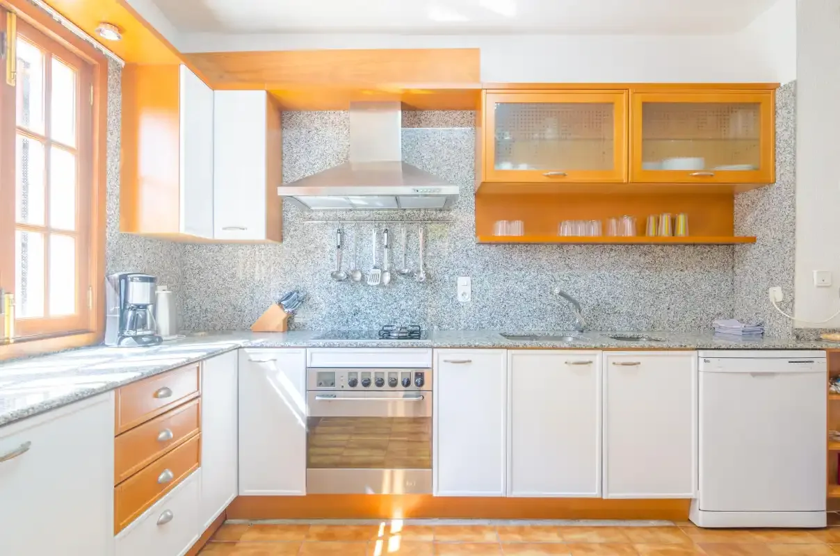A bright kitchen with white cabinets, orange trim, and a built-in oven.