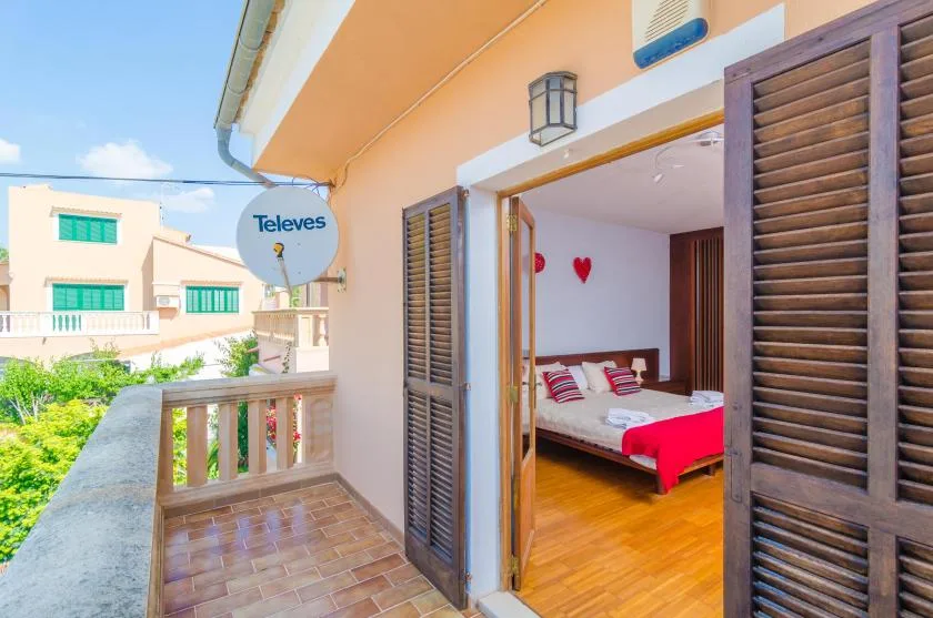 A balcony opens onto a bedroom with a bed and red bedding.