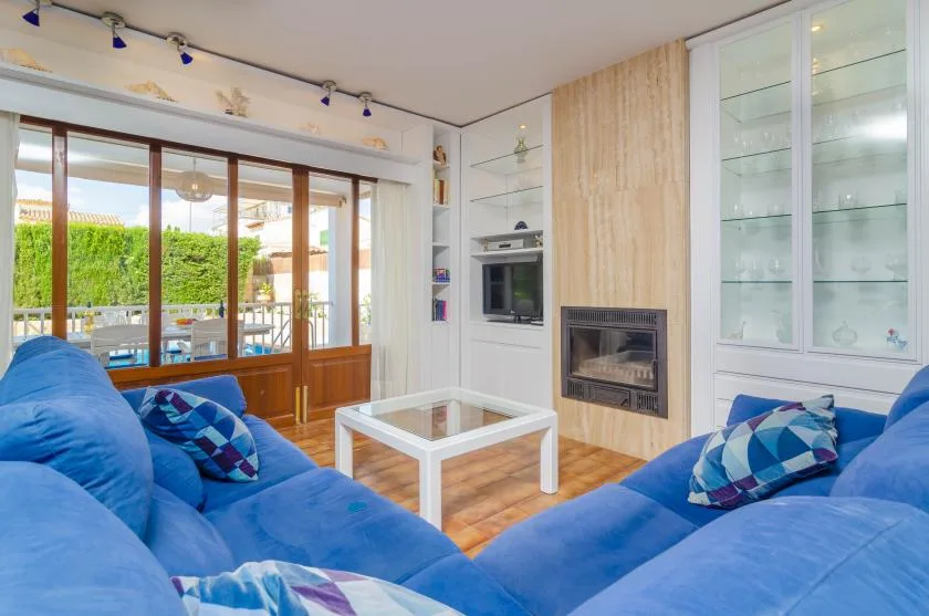 A bright living room with blue seating, a glass coffee table, and a fireplace.