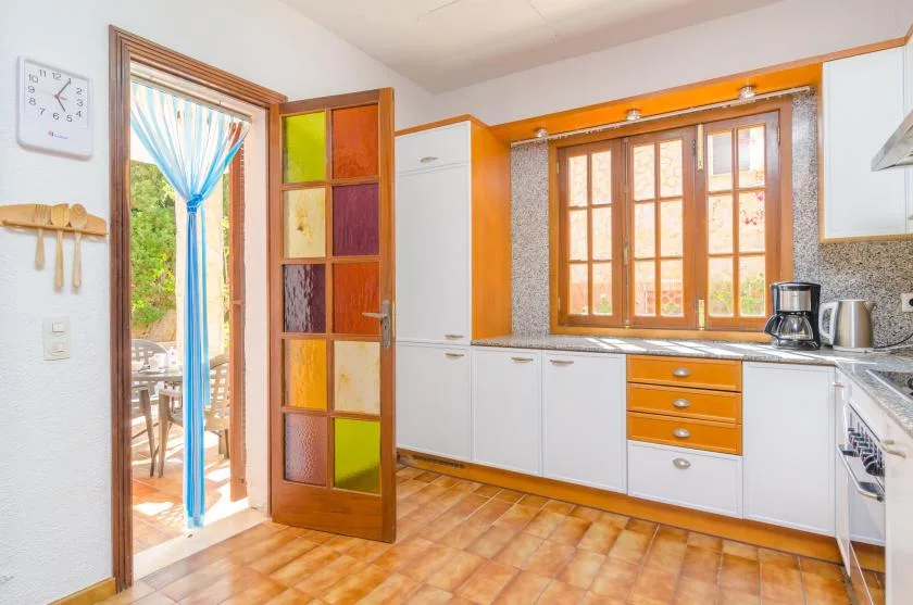 A bright kitchen with white cabinets, orange drawers, and a window above the counter.