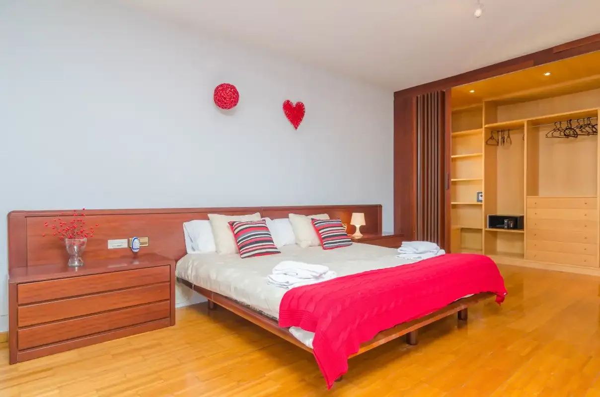 A bedroom with a wooden bed, white linens, and a bright red bedspread.